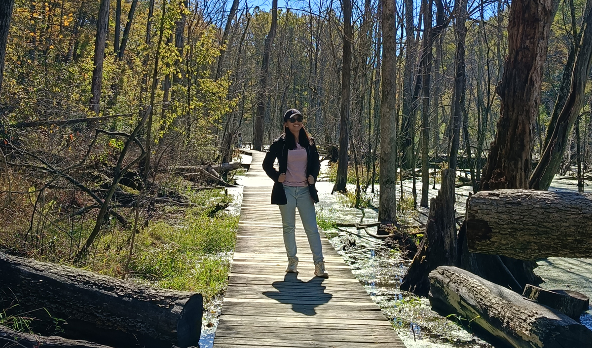 Female wearing baseball hat and sunglasses poses on a wooden boardwalk.