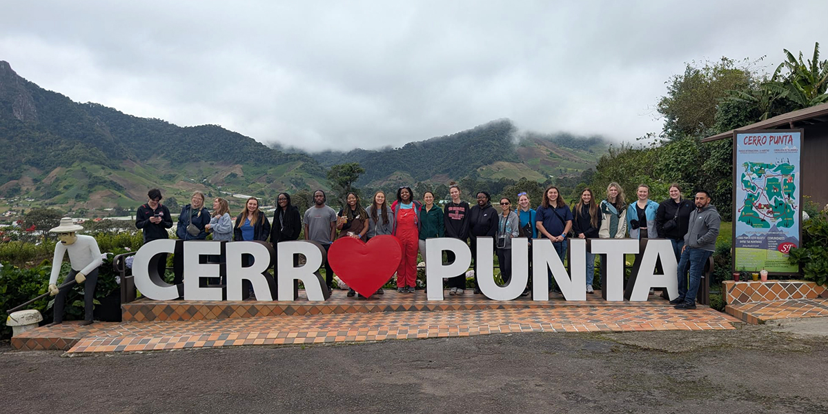 Group of people standing behind a sign that reads "CERRO PUNTA" with a red heart symbol, located in a mountainous region.