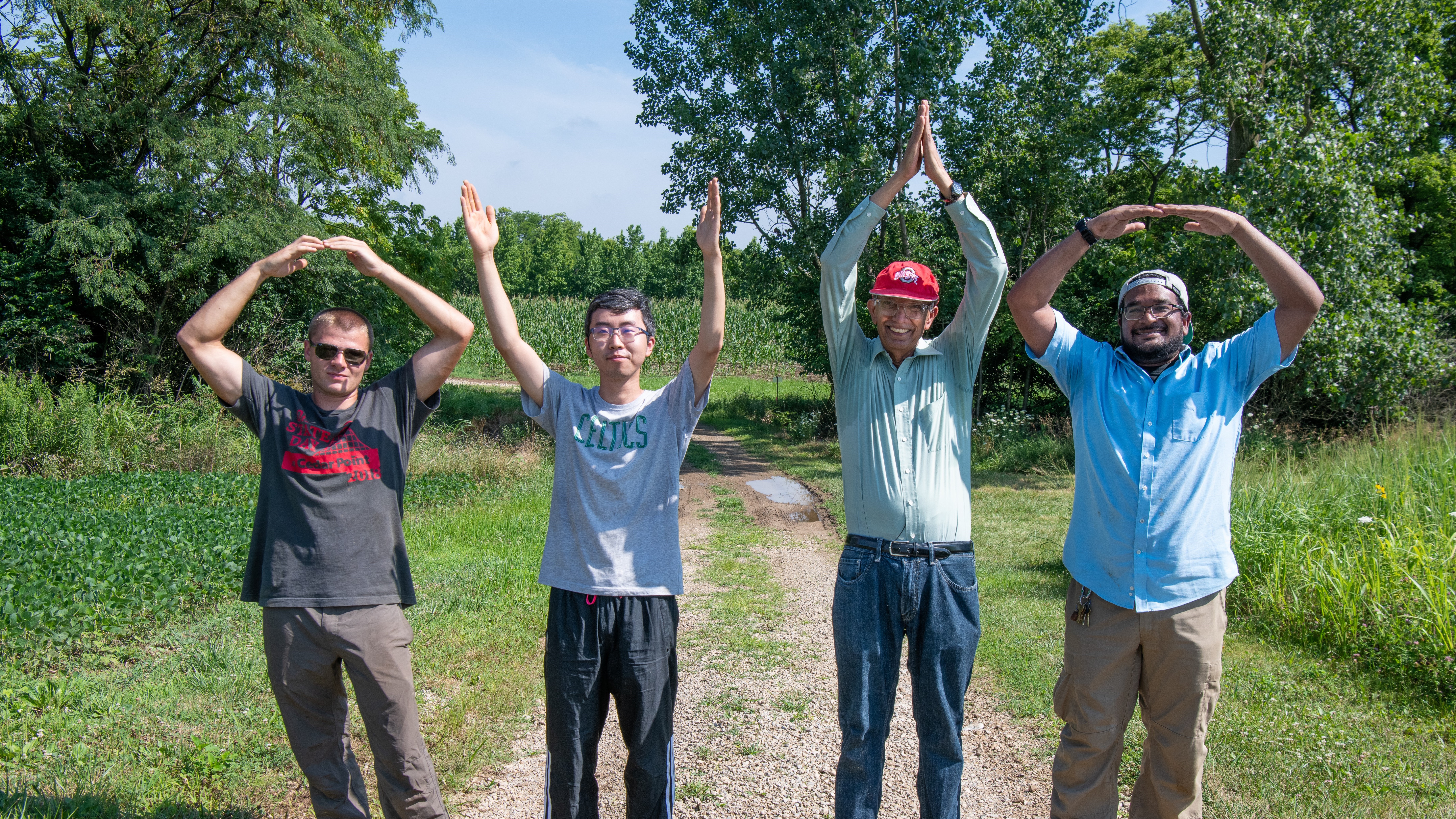 Rattan Lal poses with three students in a field doing the O-H-I-O pose