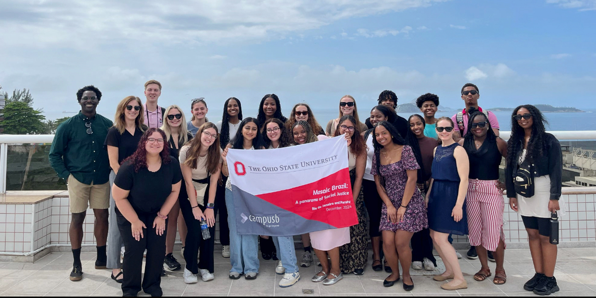 Group of Ohio State University students holding a banner, standing together on a terrace overlooking a coastal landscape.