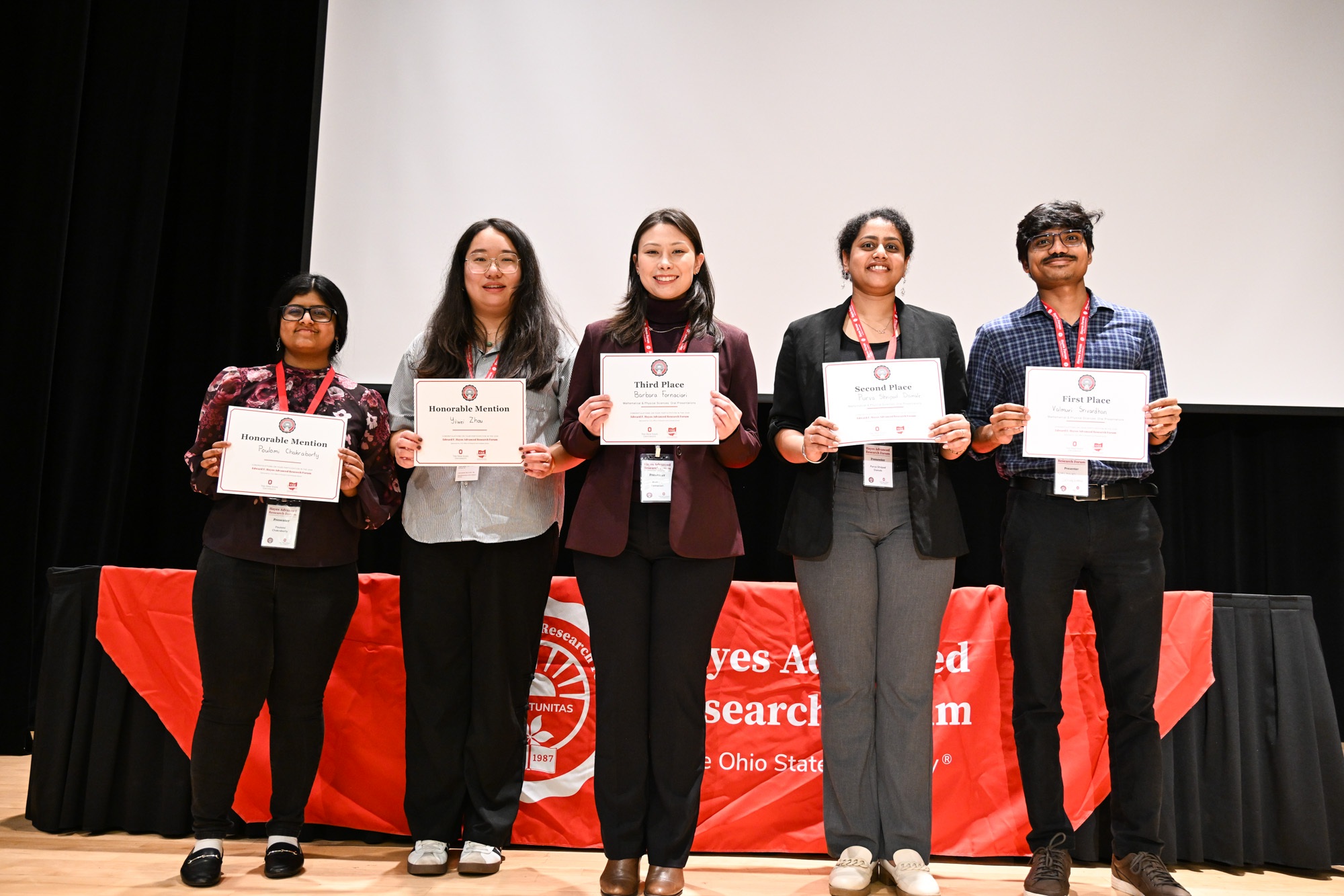 Five students holding up certificates on a stage