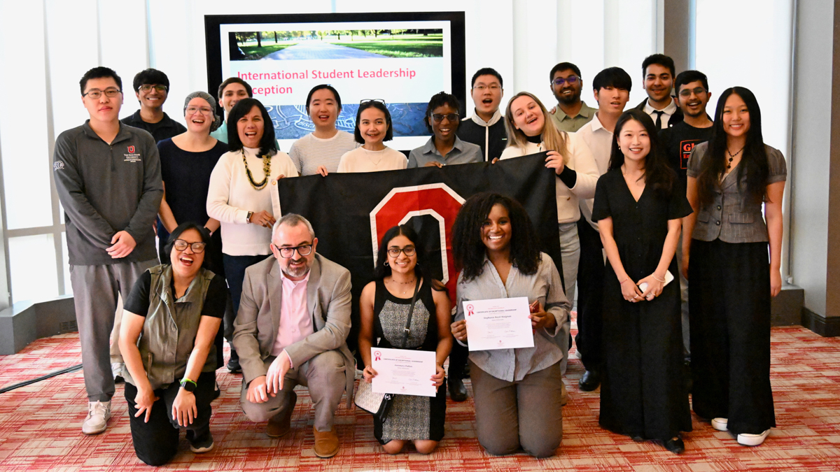 Large group of students gathered in a room with an Ohio State flag.