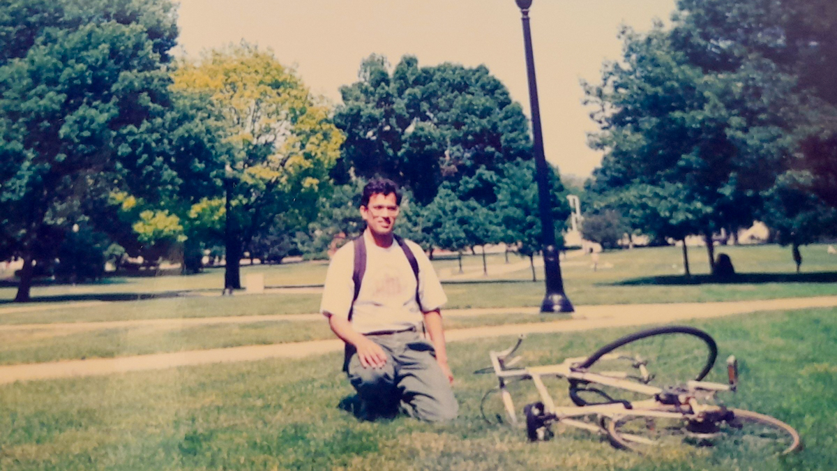 Man kneeling on ground with bicycle in foreground.