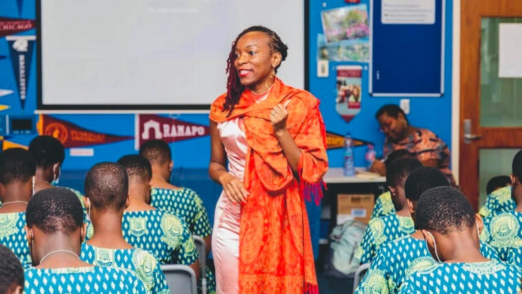 Woman in colorful clothing speaking in a classroom of children.