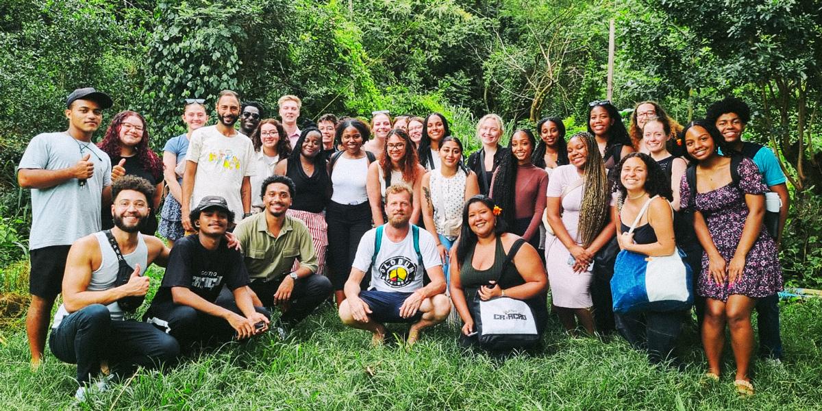 A group of diverse individuals smiling for a photo in a lush, green outdoor setting.