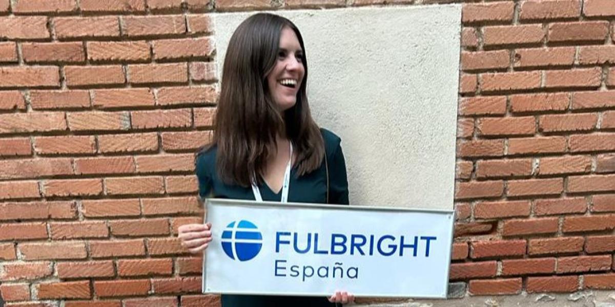 Young woman poses in front of a brick wall with Fulbright sign