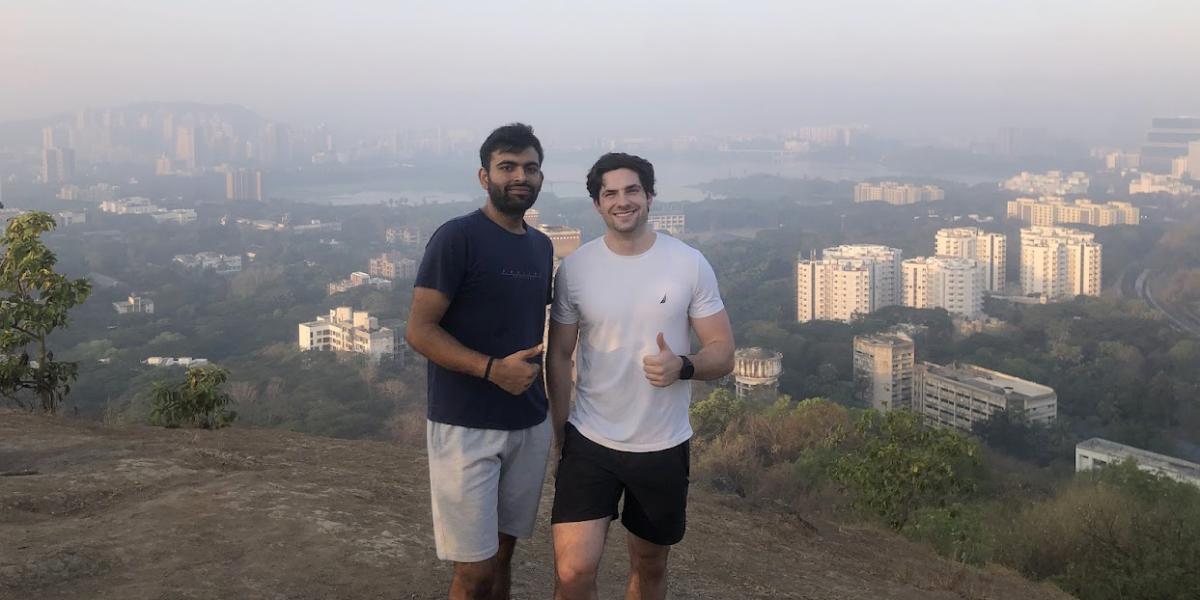 Two males on top of mountain with city background.