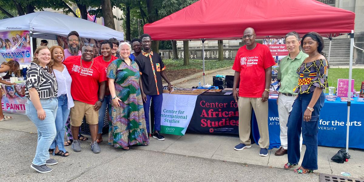 Group of people smiling at a community outreach event with booths, including one for the Center for African Studies at Ohio State.