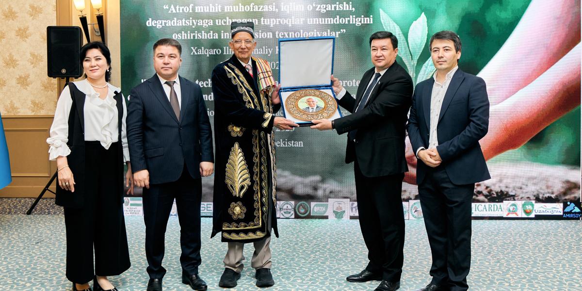Group of five individuals at a formal event, presenting an ornamental plate to a central figure, standing in front of a banner featuring logos of the Food and Agriculture Organization of the United Nations and ICARDA.