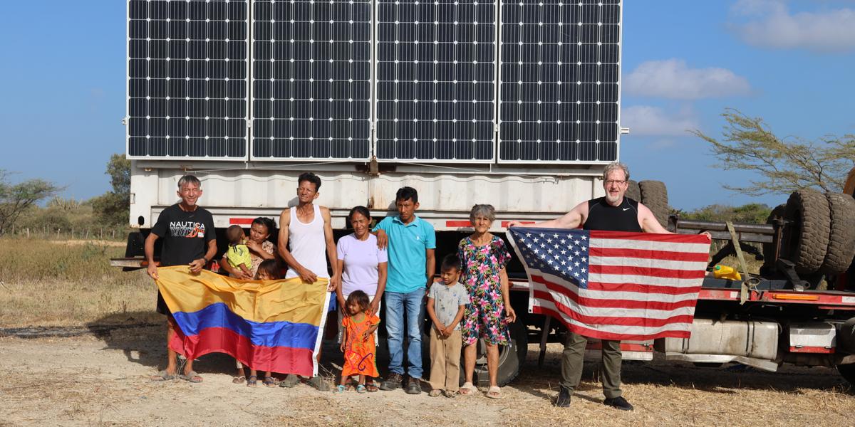 People holding Colombia and U.S. flags by solar panel.