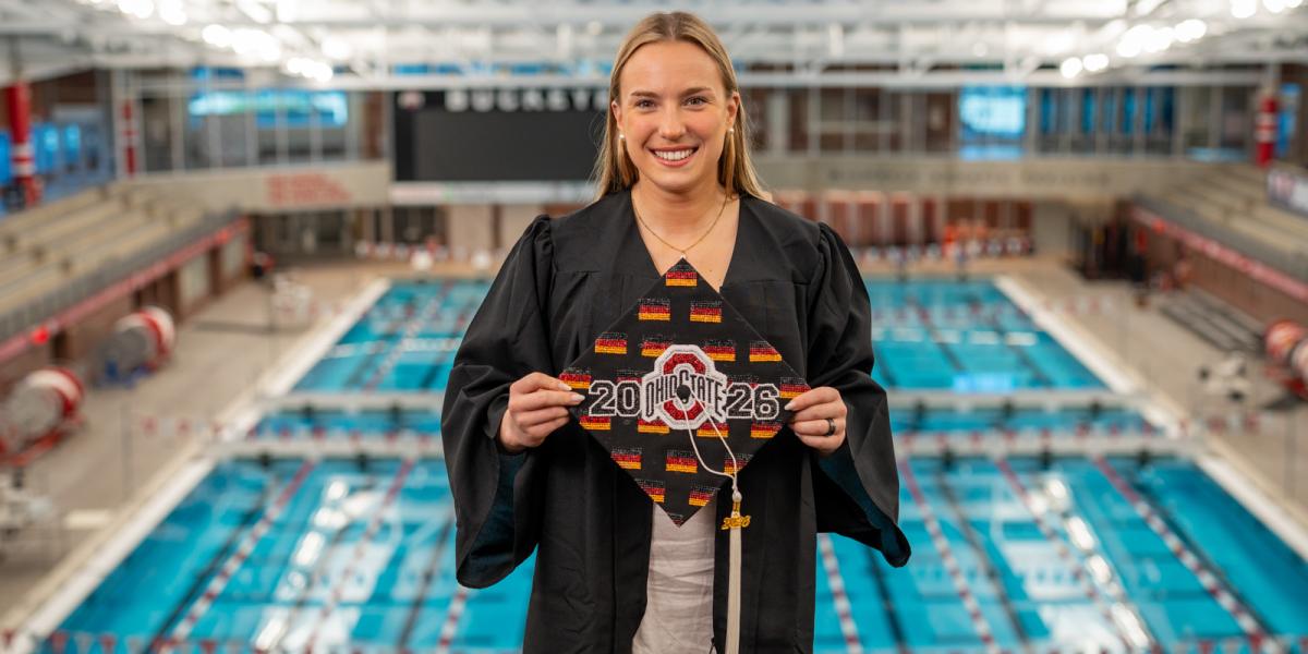 Female wearing graduation gown holding grad cap with Ohio State logo with pool in background.
