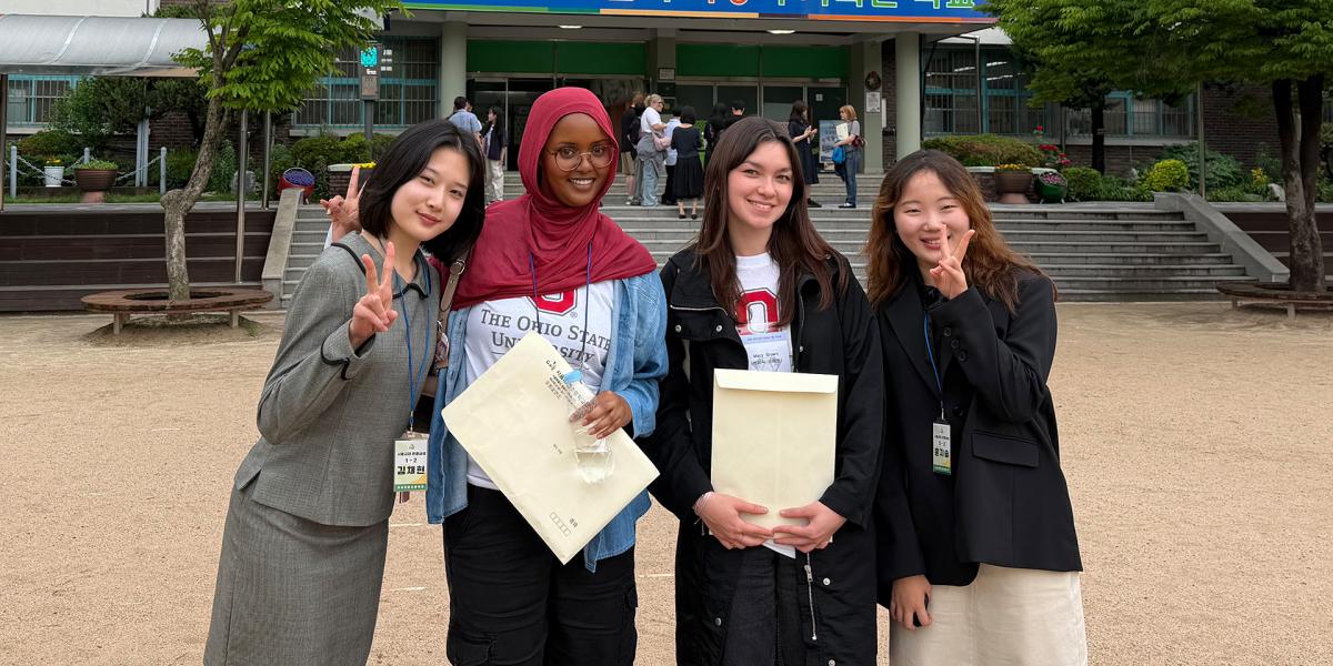 Four students stand in front of a school