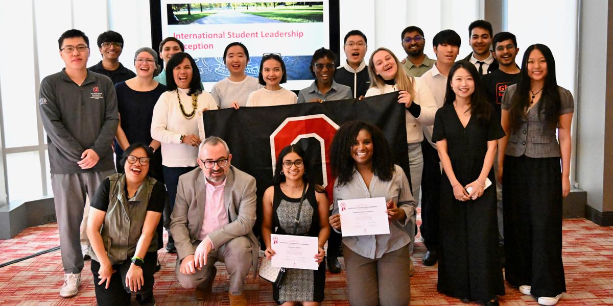 Large group of students gathered in a room with an Ohio State flag.