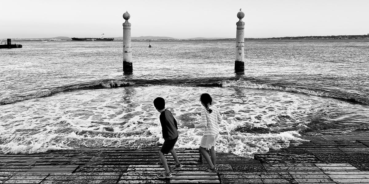 Two children playing by the edge of a lake.