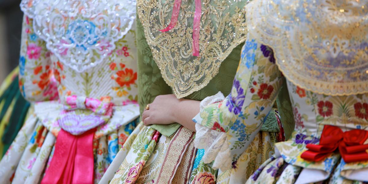 Three people in traditional Spanish dresses with elaborate lace and floral patterns during a cultural festival.