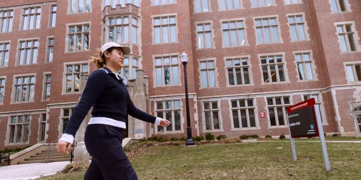 Woman walking outside in front of university building.