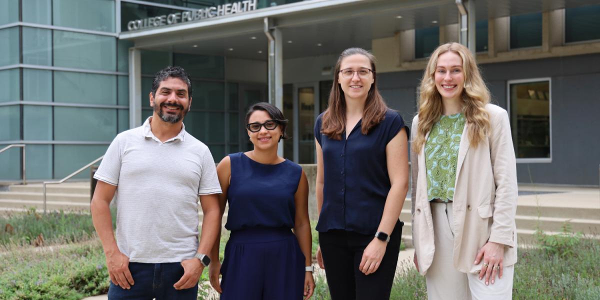 A male and three women pose outside of university building.
