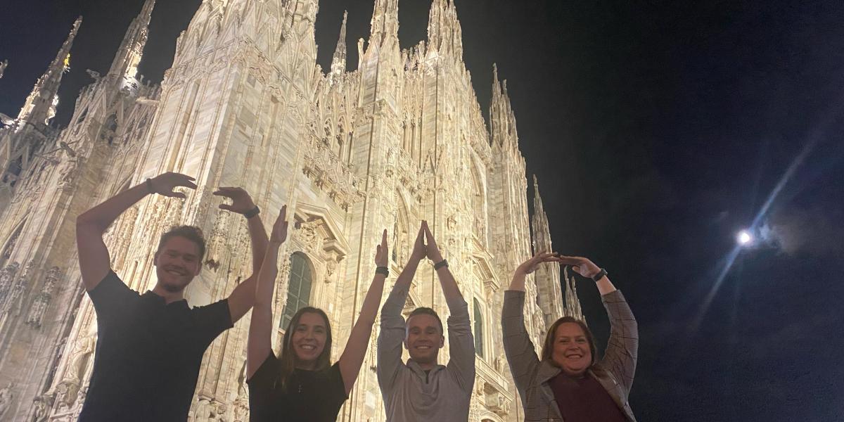 Four people do O-H-I-O in front of Italian cathedral