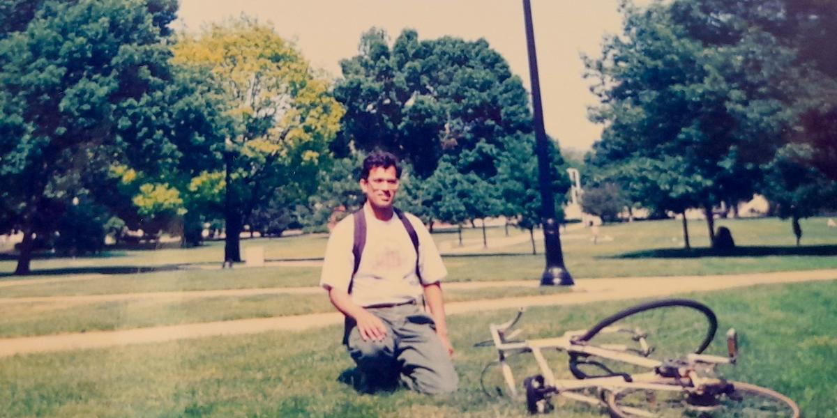 Man kneeling on ground with bicycle in foreground.