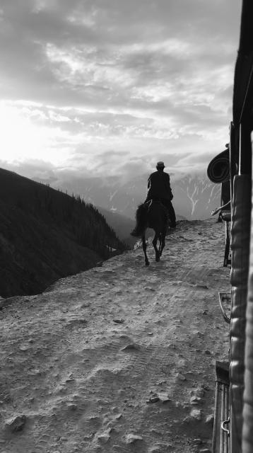 Man on horseback riding away along a trail