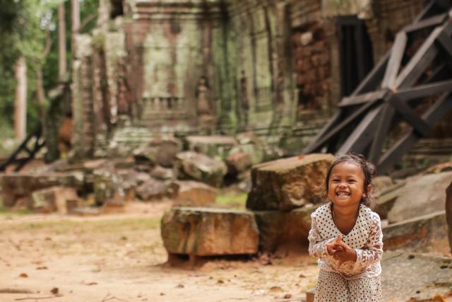 Little girl smiles for camera with Cambodian temple in background.