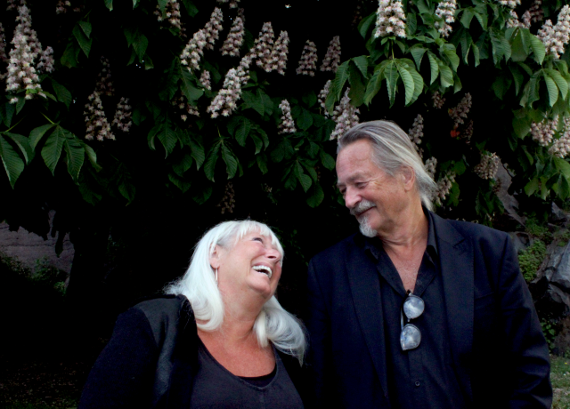 Two people smiling lovingly under a wisteria plant