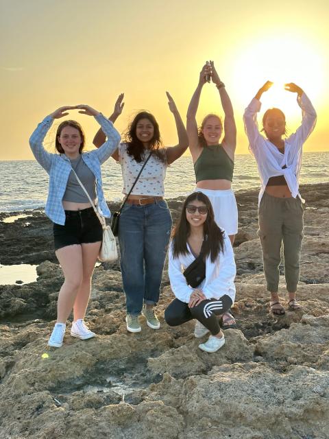 Students spell out O-H-I-O with water and sunset in background.