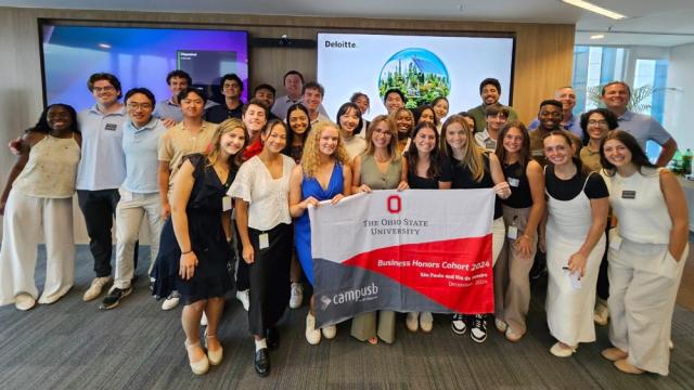 Group of students pose for photo in front of Deloitte sign