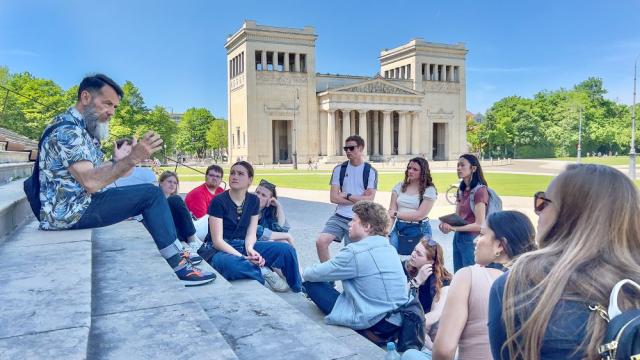 A professor speaks to a group of students on the steps of European building