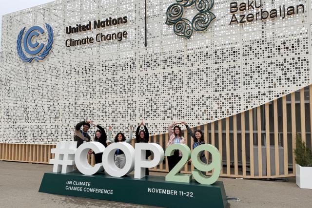 Group of individuals posing in front of the "United Nations Climate Change" sign at the COP29 event in Baku, Azerbaijan.