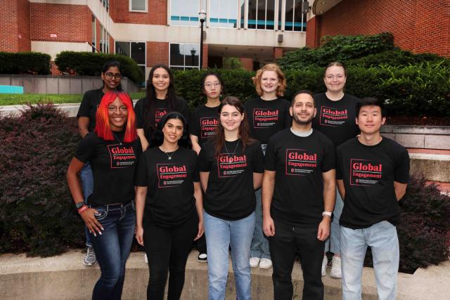 A group of students standing outside of Enarson Classroom Building smiling at the camera.