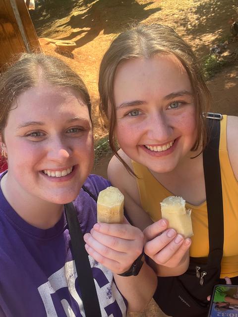 Two individuals smiling while holding ice pops in a sunny outdoor setting.