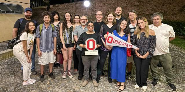Group of faculty and students holding Ohio State logo sign and pennant.