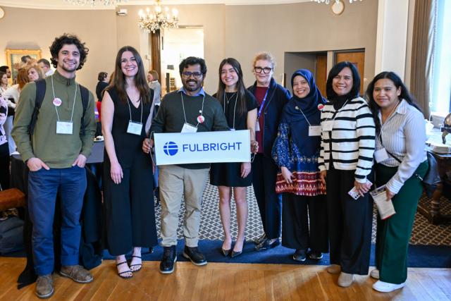Eight people pose in a line holding up a Fulbright sign.
