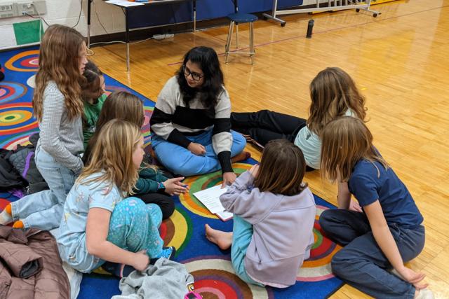 Woman sits on floor on elementary school surrounded by children