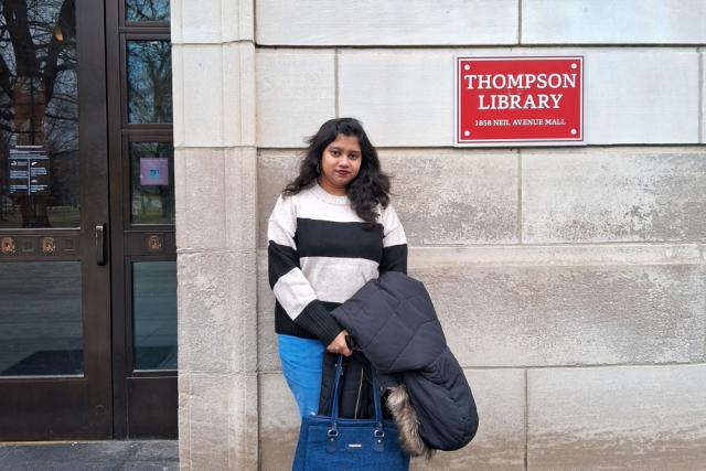 Woman leans against wall outside of Thompson Library