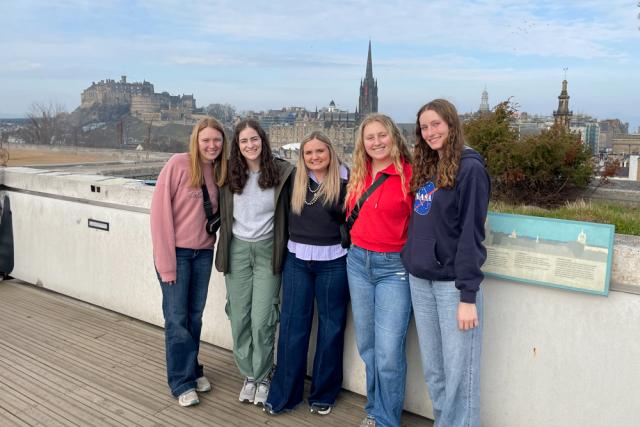 Five women posing in front of city scape.