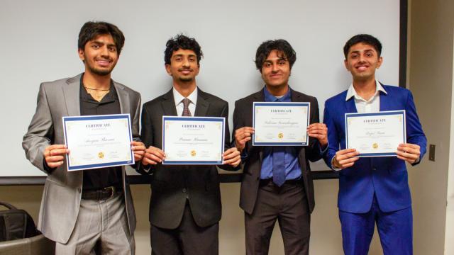 Four individuals standing in a line, each holding a certificate. They are dressed in formal attire and smiling.