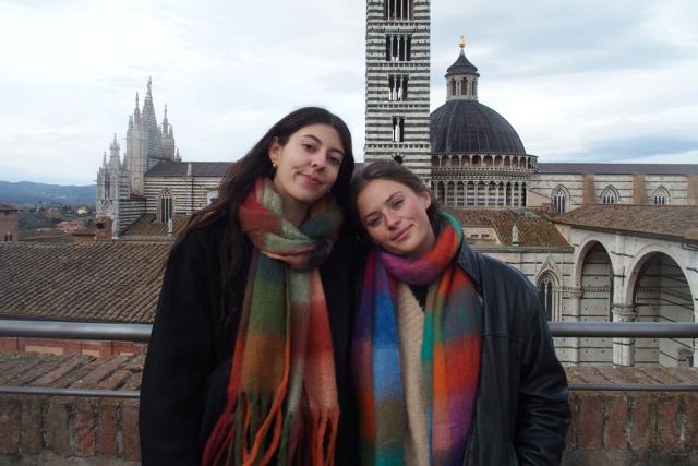 Audrey and Nicole wearing colorful scarves smiling in front of the Siena Cathedral in Italy.