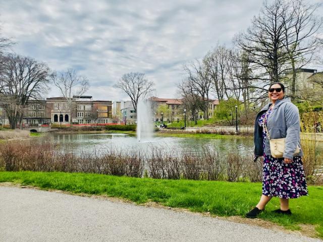 Woman stands by lake with a fountain.