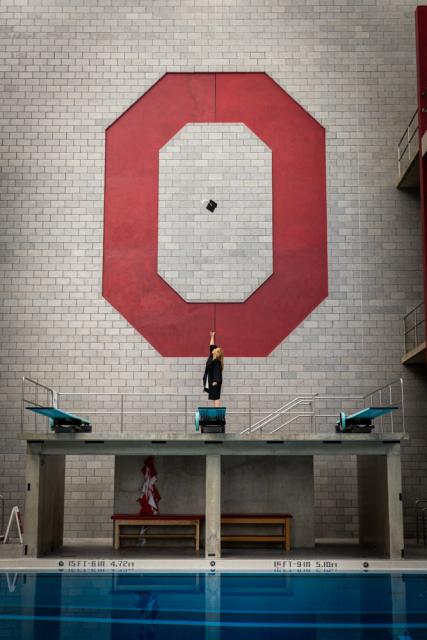 Woman standing on diving board throwing graduation cap in air.