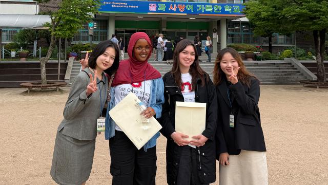 Four students stand in front of a school