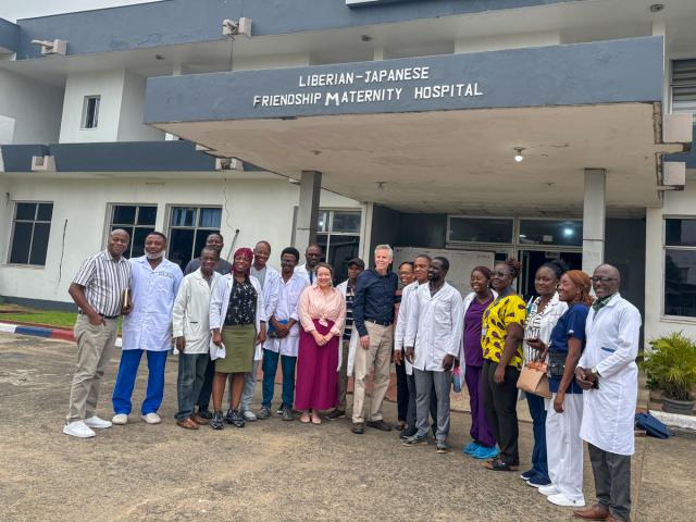 A group of people standing in front of the Liberian-Japanese Friendship Maternity Hospital. They are dressed in a mix of professional and casual attire.