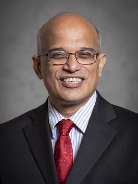 Indoor headshot of man wearing suit, red tie and glasses