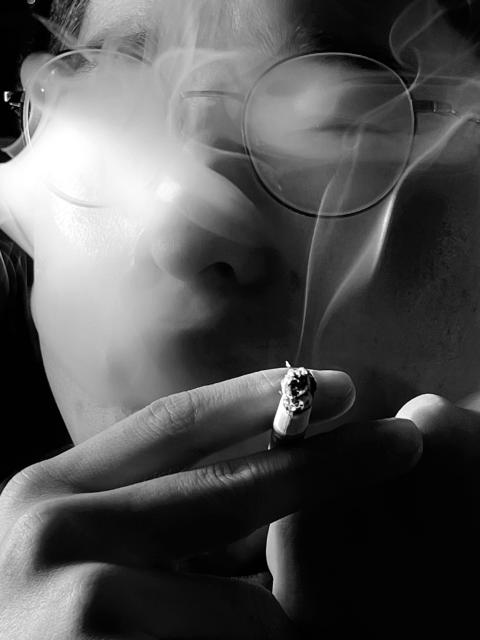 Person smoking a cigarette with smoke billowing over their glasses