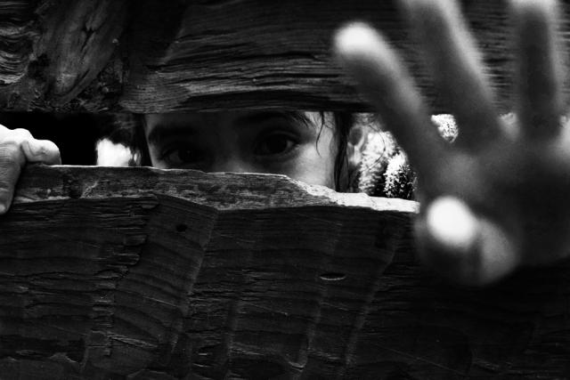 Closeup of girl looking through wood slats.