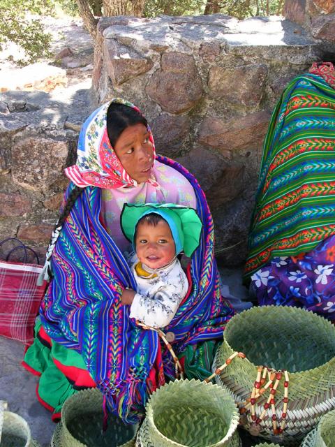 Female holding baby dressed in colorful clothing.