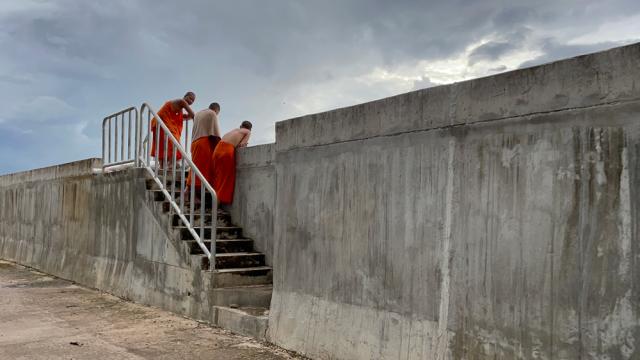 Three monks peer over a wall.