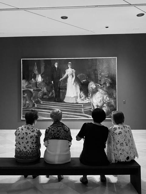 Four women sitting on a bench looking at a painting.