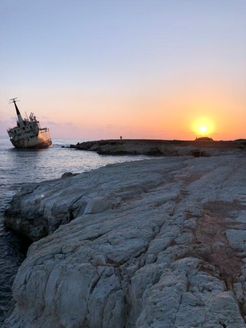 Ship tipped over in water with sunset in distance.